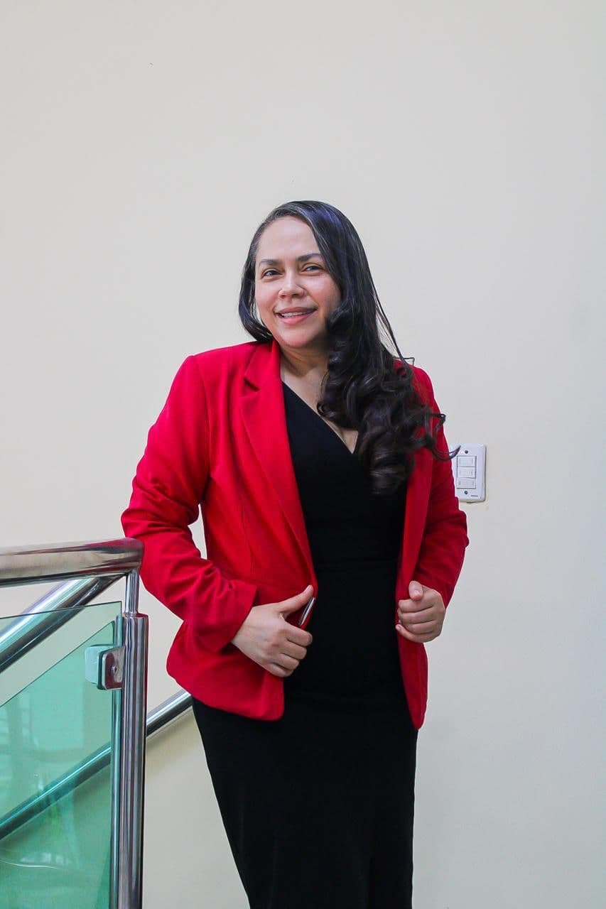 Dra. Sueli Pereira Dias, advogada, em pé, sorrindo, usando blazer vermelho sobre vestido preto.